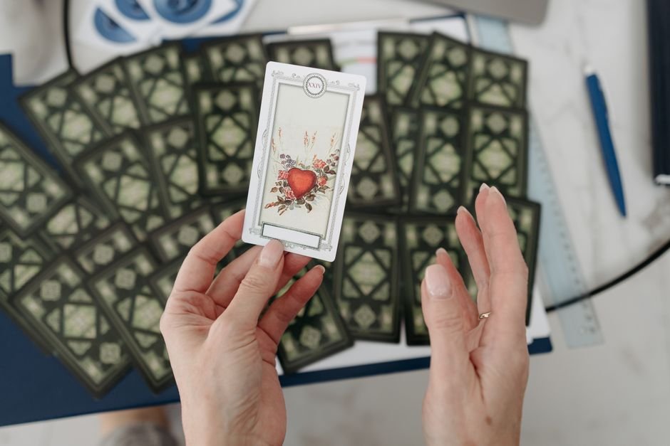 Hands holding a tarot card with heart design, surrounded by scattered cards emphasizing mystery.